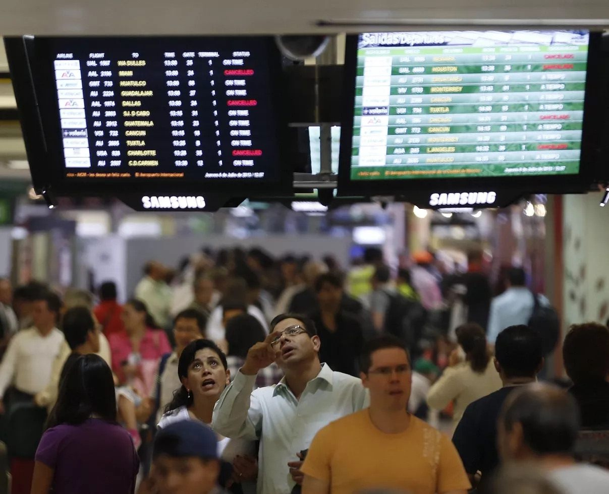 Stranded passengers look at a flight departure board after their flight was cancelled at the Benito Juarez international airport in Mexico City