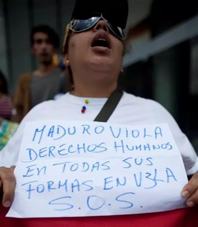 A supporter of jailed opposition leader Leopoldo Lopez holds a sign that reads in Spanish; "Maduro violates human rights in all its forms. In vigil. S.O.S.,"  joins with others outside the United Nations Program for Development (UNDP) office in Caracas, Venezuela, Friday, Sept. 26, 2014. Lopez’s wife delivered a document to the UNPD Friday, asking for the freedom of political prisoners and for respect of human rights. Lopez, who is the head of the Popular Will Party, is charged with inciting violence at early demonstrations. Before turning himself in to authorities in February, he had been spearheading a movement to force President Nicolas Maduro’s resignation. (AP Photo/Ariana Cubillos)
