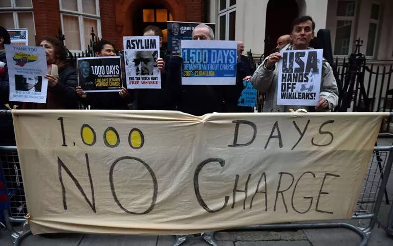 Supporters pose with placards and a banner reading '1000 days – no charge' during a vigil held for WikiLeaks founder Julian Assange outside the Ecuadorean Embassy in London on March 16, 2015, where Assange has lived since claiming refuge in 2012 to avoid extradition to Sweden, where he is wanted for questioning over sex assault allegations. Swedish prosecutors on March 13, 2015 offered to question WikiLeaks founder Julian Assange in London over rape allegations, in a U-turn that could provide a breakthrough in the deadlocked case. One of Assange’s lawyers welcomed the prosecutors' proposal, saying the interview would be a first step in clearing his client. AFP PHOTO / BEN STANSALL