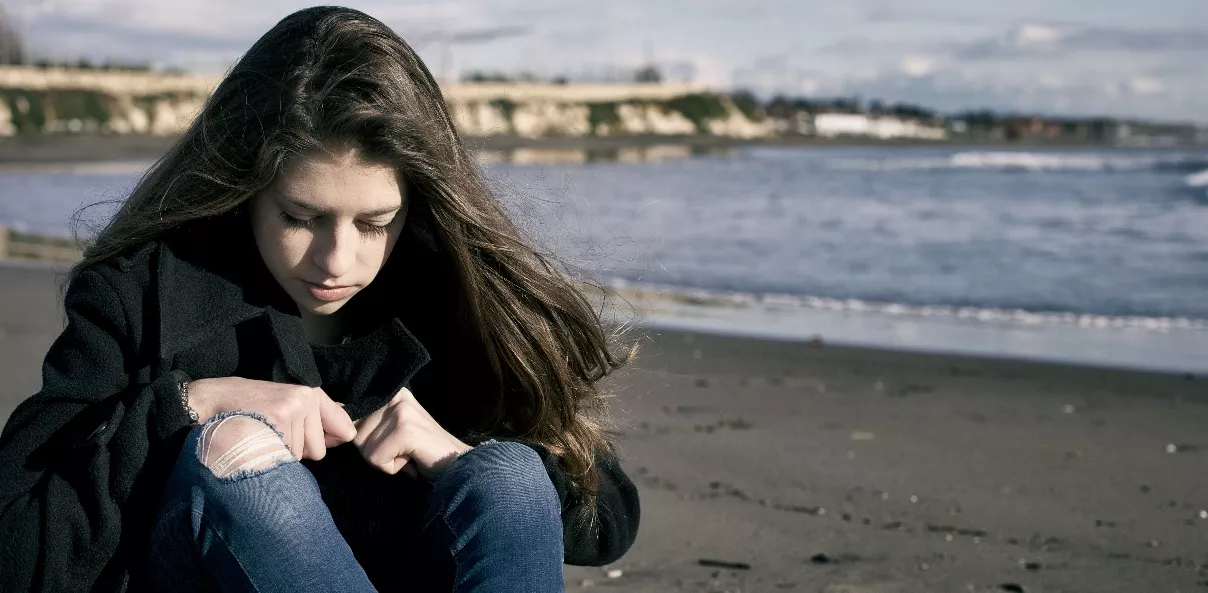 Young Female Teenager In Front Of The Storm On The Beach Sad