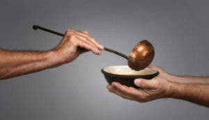 man holding a bowl in both hands, receiving a serving of soup from another man holding a soup ladle