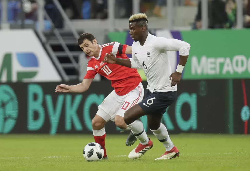 El astro francés Paul Pogba, derecha, se disputa el balón con el ruso Fyodor Smolov en un partido amistoso internacional en San Petersburgo el martres, 27 de marzo del 2018. Activistas anti racismo quieren que la FIFA investigue el acoso a jugadores franceses, incluyendo a Pogba, por fanáticos rusos. (AP Foto/Dmitri Lovetsky)