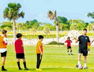 Rafael Cordero instruye a niños sobre cómo patear el balón, durante el campamento.  Fuente externa