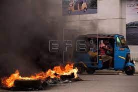 Un taximoto con algunas pasajeras pasa junto a una barricada en llamas, durante una jornada de protestas, hoy, en Cap-Haitien (Haití). EFE/Orlando Barría