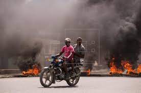 Dos hombres en motocicleta pasan junto a una barricada en llamas durante una jornada de protestas, hoy, en Cap-Haitien (Haití). EFE/Orlando Barría