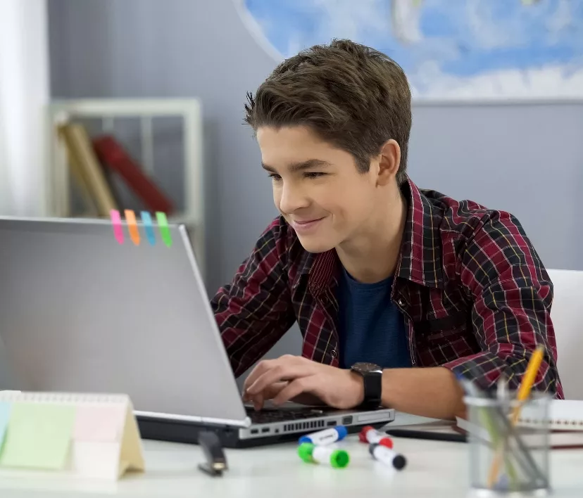 Smiling teen male chatting with friends in social networks sitting front laptop Smiling teen male chatting with friends in social networks sitting front laptop