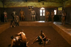 Hombres musculosos con taparrabos ajustados que se frotan tierra sagrada perfumada en los muslos y brazos combaten frente a una multitud animada, en una lucha en el barro en India.