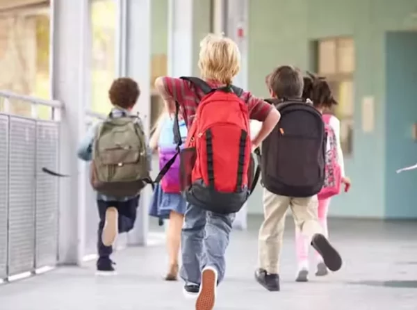Niños corriendo con mochilas en la escuela.