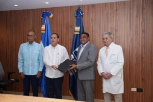 El doctor Mario Lama, director del Servicio Nacional de Salud (SNS) y el licenciado José P. Monegro, presidente del Comité Organizador de los Juegos Centroamericanos y del Caribe Santo Domingo 2026 (centro) sostienen el acuerdo firmado este lunes entre ambas entidades. En el extremo izquierdo, el doctor Melton Pinedo y en el derecho, el doctor José Joaquín Puello Herrera.