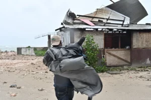Un hombre carga una lona para cubrir el techo de una casa antes del paso del huracán Melissa este lunes, en la playa pesquera de Hellshire, en Portmore
