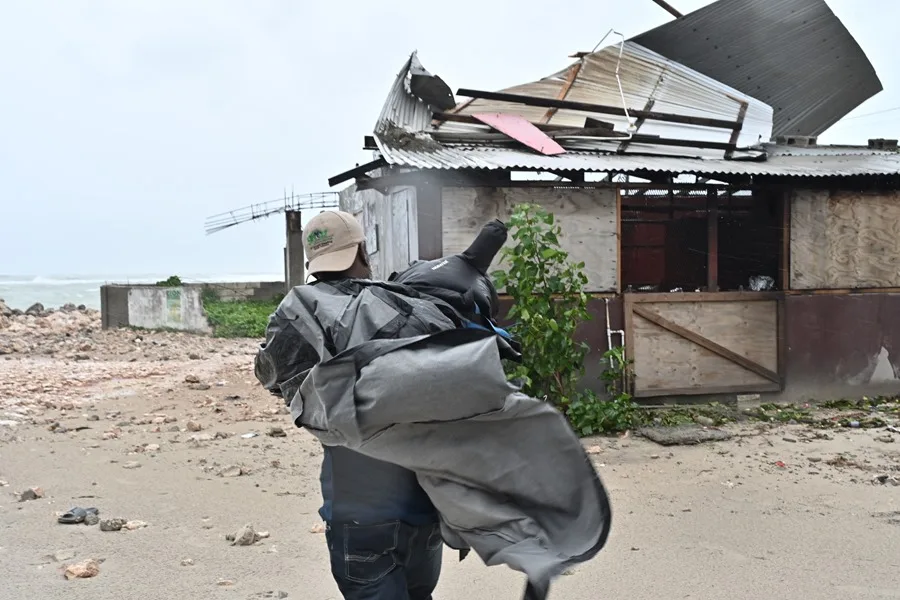 Un hombre carga una lona para cubrir el techo de una casa antes del paso del huracán Melissa este lunes, en la playa pesquera de Hellshire, en Portmore