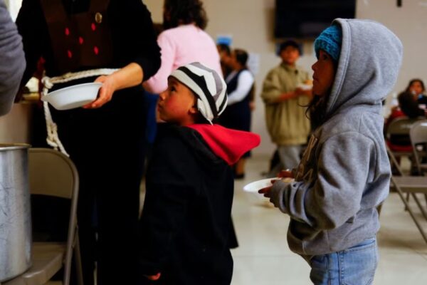 Niños migrantes de Ecuador, tratando de llegar a Estados Unidos junto con su padre, hacen fila para recibir alimentos en el comedor de una iglesia en Ciudad Juárez, México. 2023.