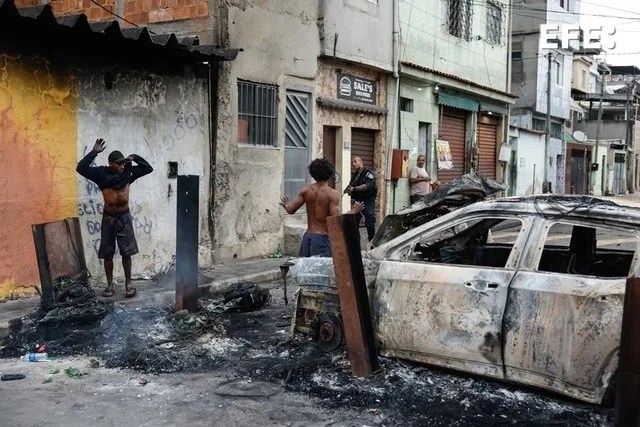 Un agente de la Policía de Río de Janeiro custodia a dos personas durante un operativo este martes contra el Comando Vermelho, una de las más poderosas bandas del crimen organizado en Brasil.