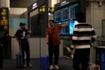 Extranjeros observan panel informativo de vuelos en el aeropuerto de Baiyun, localizado en el sur de China