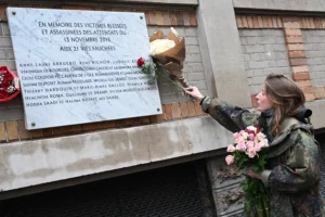 Una mujer coloca un ramo de flores sobre una placa conmemorativa frente al bar 'Belle Equipe'.