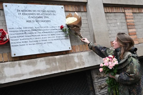 Una mujer coloca un ramo de flores sobre una placa conmemorativa frente al bar 'Belle Equipe'.