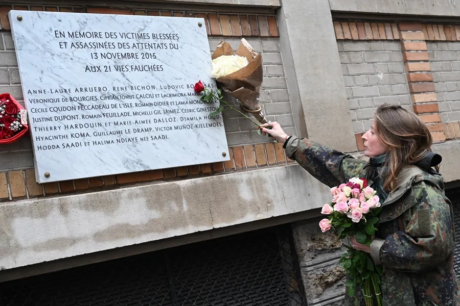 Una mujer coloca un ramo de flores sobre una placa conmemorativa frente al bar 'Belle Equipe'.