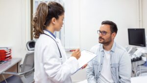 Serious man consulting with young female physician doctor at checkup meeting in hospital. Skilled general practitioner giving healthcare medical advices to patient.