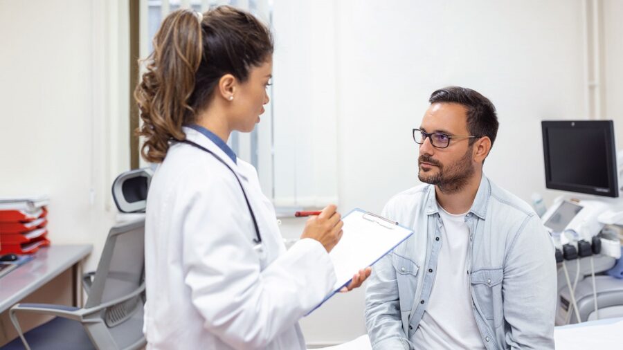 Serious man consulting with young female physician doctor at checkup meeting in hospital. Skilled general practitioner giving healthcare medical advices to patient.