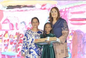 Alicia Quijano y  Nancy de Menicucci entregan un reconocimiento  a Isabella Sophia Díaz.