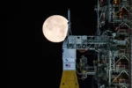 La Luna llena se ve sobre la nave Orion en el Sistema de Lanzamiento Espacia (SLS, por sus siglas en inglés) en la plataforma en las primeras horas del domingo 1 de febrero de 2026, en el Centro Espacial Kennedy en Florida. (