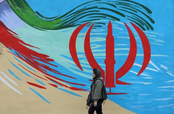 Fotografía de archivo de una mujer caminando frente a un mural con la bandera iraní, en Teherán (Irán).