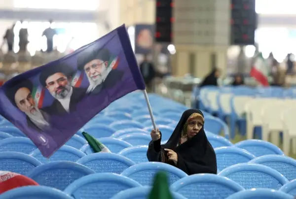 Una mujer iraní sostiene una bandera con los retratos de los difuntos líderes supremos y el actual, en una ceremonia en memoria de los caídos en la guerra con EE.UU. e Israel, celebrada el domingo en la mezquita de Mosallah en Teherán.
