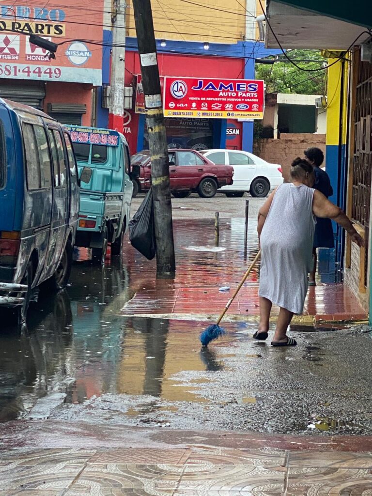 Mujer barre agua frente a su vivienda en la avenida Duarte.