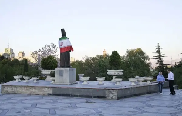 Una pareja charla frente a la estatua de un poeta persa cubierta con una bandera de la República Islámica en un parque de Teherán. EFE/Jaime León