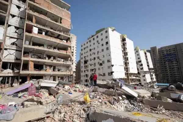 Fotografía de personas caminando entre escombros de edificios afectados por terremotos, en Catia La Mar, La Guaira (Venezuela).