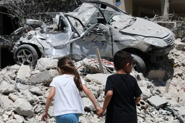 Fotogafía de archivo del 15 de junio de 2026 de niños caminando frente a vehículos dañados y escombros tras un ataque israelí, en Maaroub (Líbano).