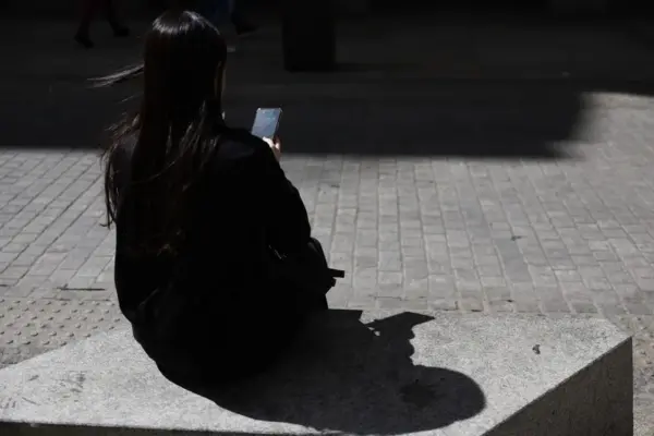 Una joven descansa sentada en un banco en la calle mientras mira su teléfono móvil.
