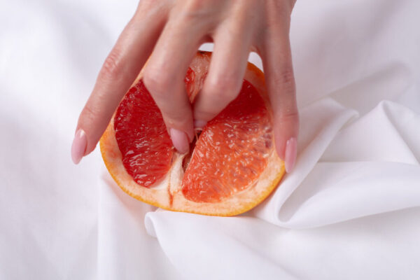 Female hand and half of juicy grapefruit on white background. Erotic concept