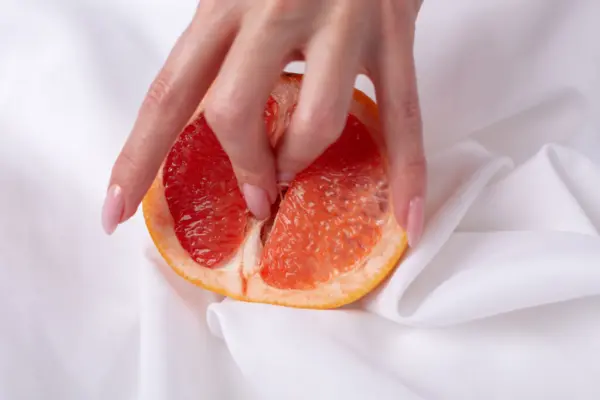 Female hand and half of juicy grapefruit on white background. Erotic concept