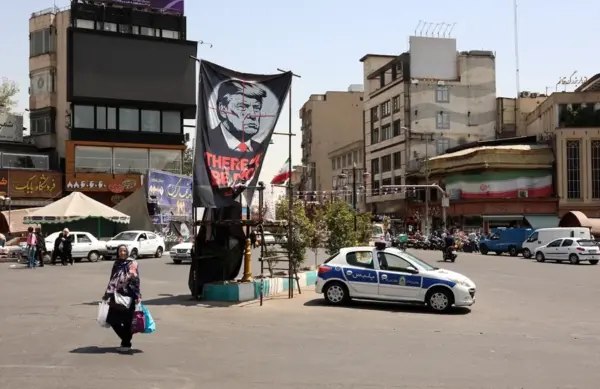Una mujer iraní camina con sus bolsas de la compra junto a una pancarta antiestadounidense, en Teherán, Irán,.