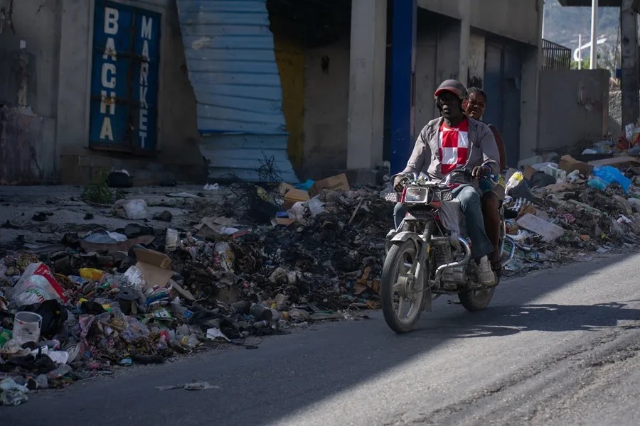 personas movilizándose en una motocicleta por una calle cubierta de basura, en Puerto Príncipe (Haití).